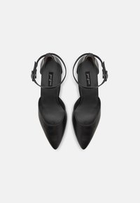 Černé lodičky s špičatou špičkou a hladkým koženým svrškem, vybavené nastavitelným páskem kolem kotníku a plochou podrážkou. Minimalistický design, bez ozdob.