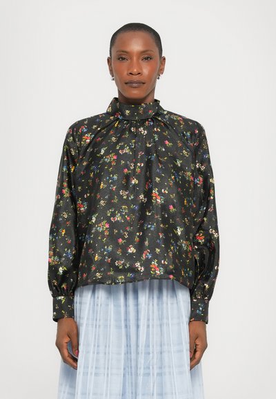 Schwarze Bluse mit floralen Mustern, langen Puffärmeln, hohem Kragen und mehrfarbigem Blumenmuster; satinähnliche Textur. Getragen über einem hellblauen, gefalteten Rock.