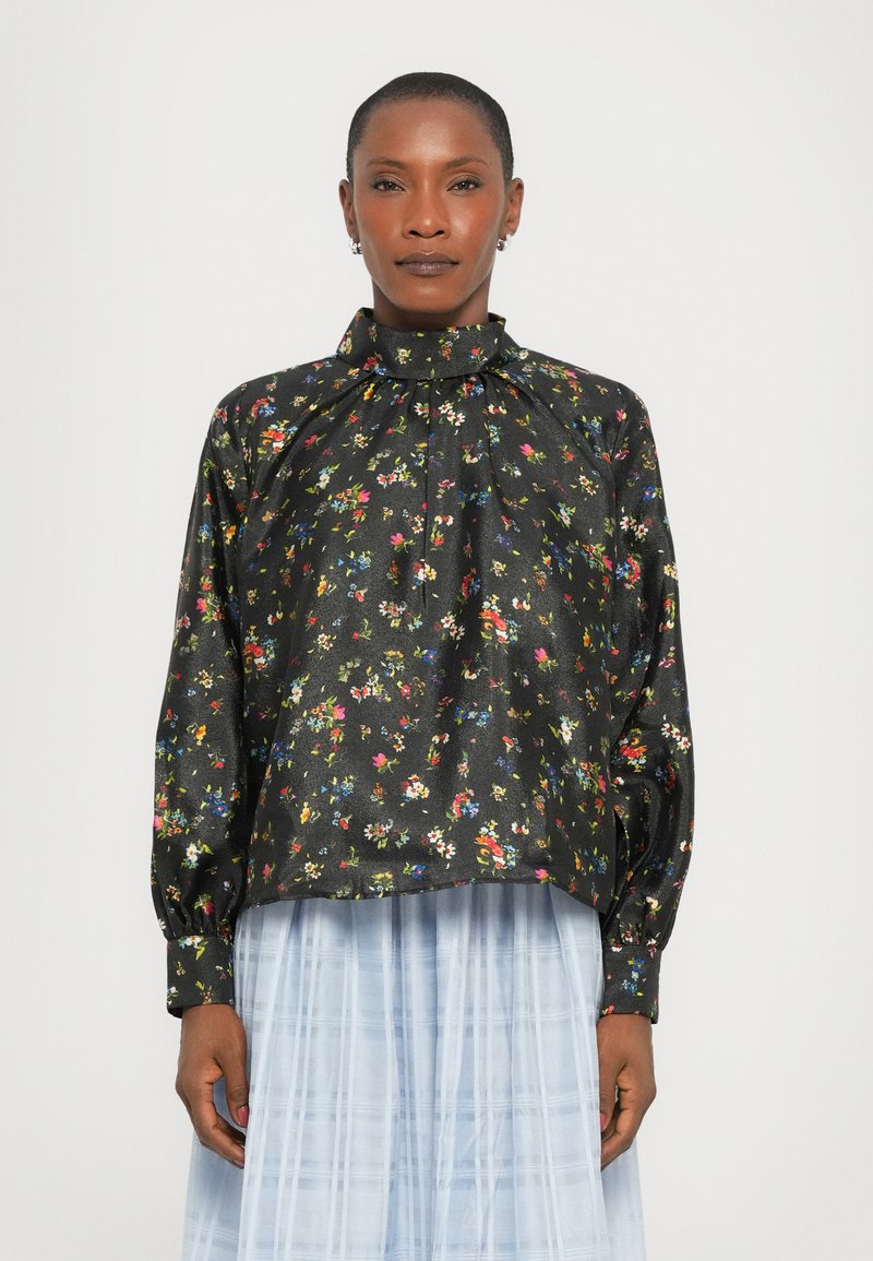 Blusa nera floreale con maniche a sbuffo lunghe, colletto alto e motivo floreale multicolore; tessuto in satin. Indossata su una gonna plissettata azzurro chiaro.