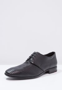 Chaussure à lacets noire avec un motif texturé, un bout pointu élégant et un petit talon noir. Finition en cuir lisse avec un accent de marque subtil.