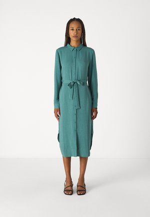 Teal button-up dress with long sleeves and a tie waist belt. Made of soft fabric, features side slits, and a straight silhouette. Black sandals.