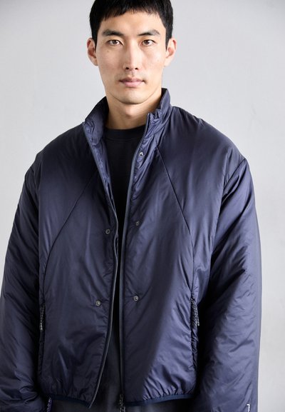 Giubbotto imbottito blu navy con colletto alto, maniche raglan, chiusure con zip e bottoni a pressione, e tasche laterali. Tessuto liscio e trapuntato.