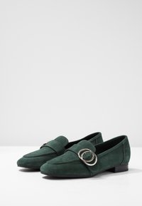 Mocassins en daim vert avec un bout pointu et deux accents métalliques circulaires, dotés de détails de couture et d'un petit talon empilé.