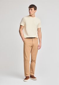 Beige katoenen T-shirt, khaki broek, bruine sneakers. Eenvoudig ontwerp, korte mouwen, goed passend, met een gladde textuur en minimale branding.
