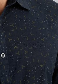 Chemise marine avec des motifs géométriques en olive et blanc. Col boutonné, tissu tissé et logo brodé sur la poitrine.
