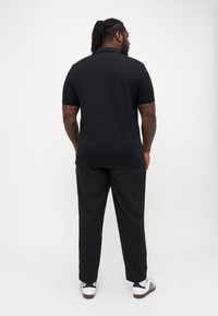 Sort kortærmet polo-shirt med krave, parret med sorte bukser og hvide sneakers med sorte og brune detaljer.