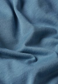 Miękka, teksturowana tkanina w stonowanym niebieskim odcieniu, z gładkim splotem i widocznymi włóknami oraz delikatnym układaniem. Idealna do różnych zastosowań odzieżowych.