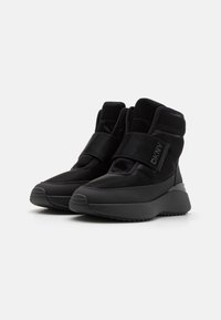 Sorte ankelboots med en glatt nylonoverdel, bred borrelåsrem og en tykk, teksturert såle. Minimalistisk design med DKNY-merke.