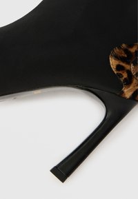 Bottine noire à talons hauts au design élégant, avec un accent en imprimé léopard et une texture lisse. Talon robuste avec une base carrée.