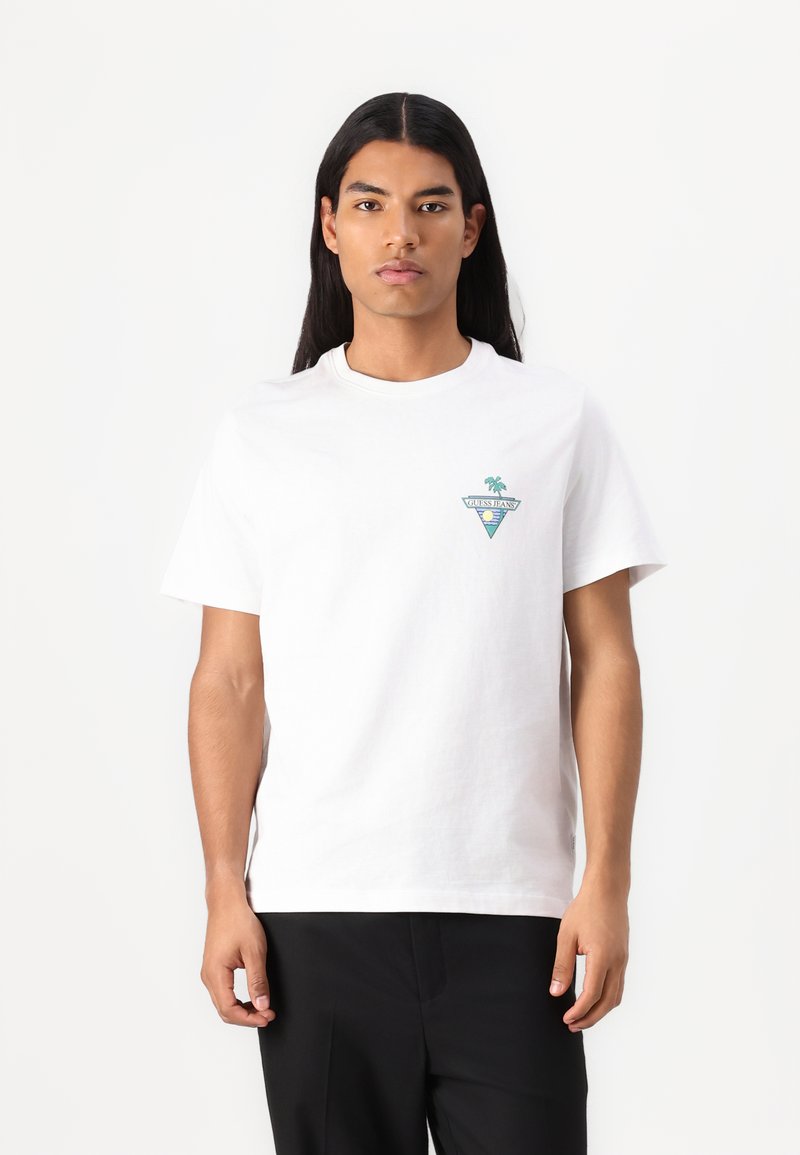 T-shirt en coton blanc avec un col rond, des manches courtes et un petit graphique de palmier teal et jaune dans un design triangulaire sur la poitrine.
