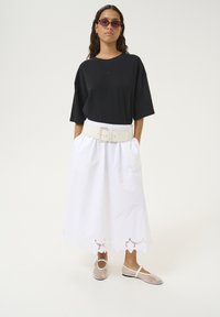 Sort oversized t-shirt, hvid ankellang nederdel med bølget kant og gennemsigtige slip-on sko. Tilbehør med lilla solbriller.