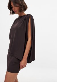 Hnedé šaty so zavesením a krátkou sukňou, s vysokým golierom a otvorenými rukávmi, vyrobené z hladkej látky s módnou textúrou.