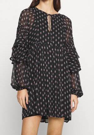 Vestido mini negro transparente de manga larga con pequeños patrones florales en blanco y rojo, mangas en capas con volantes y escote con lazo en la parte delantera.