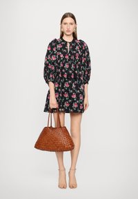 Svart blomsterkjole med puffermer og nøkkelhals, kombinert med en stor vevd brun håndveske og sandaler med stropper i beige.