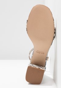 Sandale à talons hauts avec un motif en cuir de serpent, présentant une semelle beige, des accents tissés et un design de bride. Surface texturée avec un talon robuste.