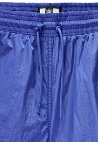 Blå shorts med elastisk talje og snor. Lavet af glat, let materiale med en let glans. Ingen synlige lommer.