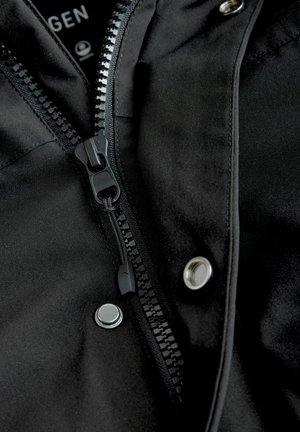 Chaqueta negra con cremallera central y botones a presión, hecha de un tejido suave con textura mate, que presenta costuras y herrajes detallados.