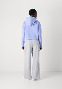 Un sweat à capuche court de couleur violet clair avec une capuche à cordon et un ourlet côtelé, associé à un pantalon de jogging ample gris et des baskets blanches.