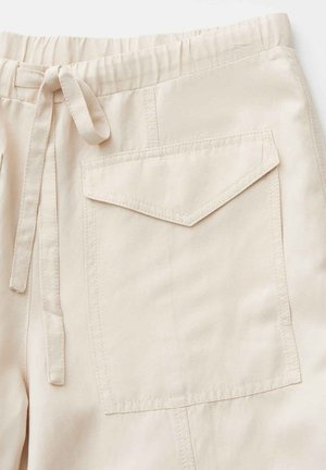 Pantalon en tissu beige avec taille élastique, cordon de serrage en tissu et grande poche rectangulaire avec rabat sur le côté droit.