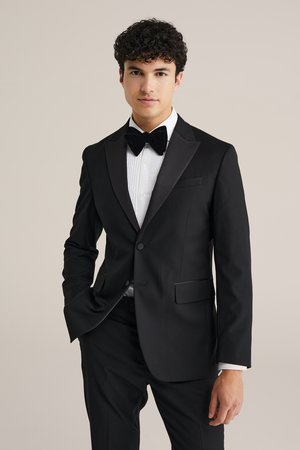Černý smoking se saténovými klopami a bílou nápadně skládací košilí. Obsahuje černý motýlek. Hladký materiál s přizpůsobeným střihem.