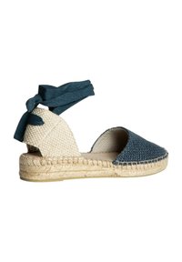 Espadrilles trenzadas azules con suela de yute beige, lados abiertos y una correa de tela atada en el tobillo. Parte superior texturizada y detalles de yute trenzado.