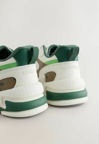 Par atletskih čevljev v zeleni in beli barvi, videnih od zadaj, z debelimi podplati in povlečnimi zankami na petah.