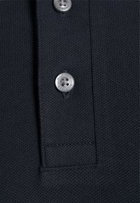 Polo de color azul marino con textura de punto, que presenta dos botones plateados y un pequeño bolsillo. Los detalles de costura son visibles a lo largo de los bordes.