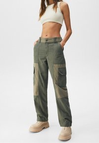 Kargo kalhoty v olivově zelené barvě s béžovými akcenty, s vysokým pasem, bočními kapsami a uvolněným střihem. Vyrobeny z bavlněné směsi.