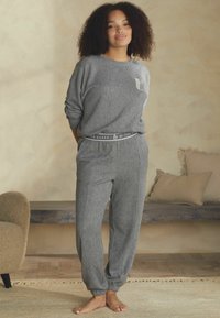 Šedý žebrovaný loungewear set s kulatým výstřihem a kapsou na horní části, elastickým pasem na kalhotách a zúženými manžetami, předvedený na modelce.