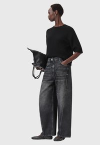 Maglione nero a costine con maniche corte, abbinato a jeans in denim di un grigio scuro oversize. Indossato con scarpe ballerine nere con borchie e una borsa nera.