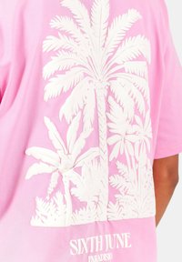 Roze t-shirt met korte mouwen, featuring witte reliëf palmboomontwerpen en merknaam "SIXTH JUNE" onderaan. Glad katoenen textuur.