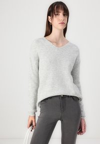 Light grey, ribbed knit sweater with a V-neck and long sleeves, paired with dark grey jeans. The sweater has a relaxed fit and soft texture.