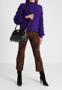 Fioletowy sweter na drutach z teksturowanymi, bufkami przy rękawach, zestawiony z brązowymi spodniami w panterkę i czarnymi botkami na wysokim obcasie. Akcent w postaci czarnej torebki.