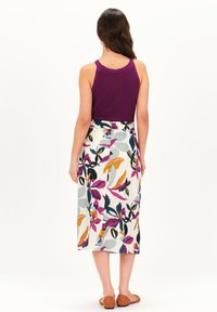 Top de tirantes morado de canalé combinado con una falda blanca hasta la rodilla que presenta un vibrante estampado floral en tonos rosas, naranjas y azules. Sandalias marrones.