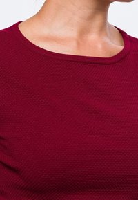 Top bordeaux texturé avec un col rond, présentant un délicat motif alvéolé et une finition en tissu lisse.