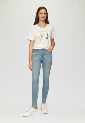 Weißes kurzärmeliges T-Shirt mit einem Linienstil-Design, kombiniert mit hellblauen engen Jeans und klobigen weißen Turnschuhen. Glatte Baumwolltextur.