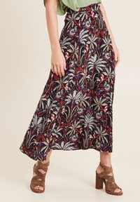 Lange, vloeiende zwarte rok met een kleurrijk bloemenpatroon. Heeft een hoge tailleband en wordt gecombineerd met bruin, gespsandalen.
