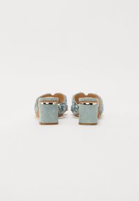 Blauwe suede blokhak muiltjes met decoratieve bloemversieringen, open achterkant en ronde neus. Platte zool voor stabiliteit.