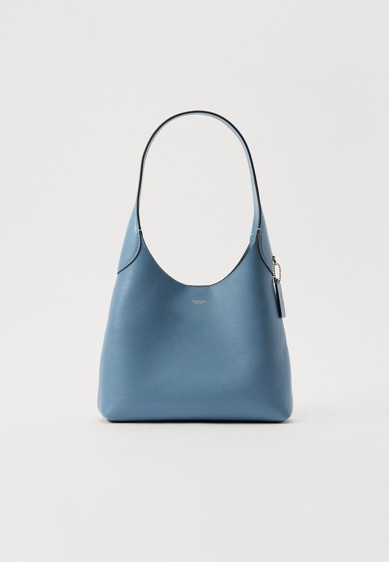 Mala de couro azul com uma textura suave, forma curva e uma alça única para o ombro. Apresenta um pequeno detalhe de logotipo e um fecho com zíper.