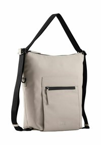 Beige Umhängetasche aus glattem Material, mit einem schwarzen Schulterriemen, einer vorderen Tasche mit Reißverschluss und minimalistischen Designelementen.