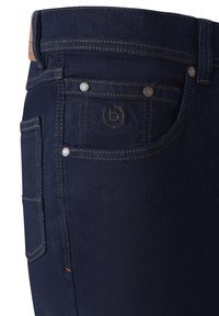 Dunkelblaue Denim-Jeans im Nahaufnahme, die die Vordertasche mit kleinem geprägt Logo und sichtbaren Nähdetails zeigen.