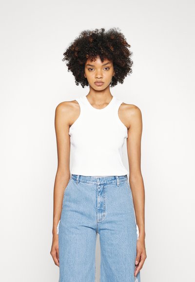 White sleeveless top with a rounded neckline, paired with high-waisted light blue wide-leg jeans featuring a distressed accent.