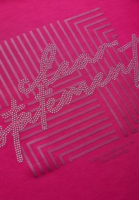 Tissu fuchsia avec un design graphique présentant des lettres en relief entourées de strass et des motifs linéaires géométriques ; texte en relief en dessous.