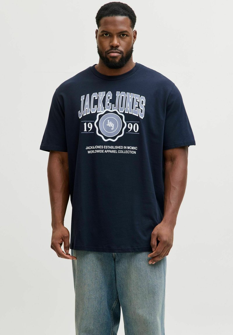 Tumši zils kokvilnas T-krekls ar uzrakstu baltā krāsā "JACK & JONES 1990" un logo. Ar īsām piedurknēm un brīvu piegriezumu.