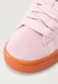 Baskets en suede rose avec lacets tressés, dotées d'une semelle en caoutchouc texturée de couleur orange. Embout arrondi et coutures décoratives sur le dessus.