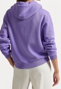 Felpa viola realizzata in materiale morbido, con cappuccio regolabile, polsini e vita a coste, dal fit rilassato e finitura testurizzata.