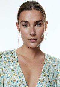 Blumenmusterkleid mit kleinen gelben und blauen Blumen auf einem hellen Stoff, mit einem V-Ausschnitt und weichem, strukturiertem Material.