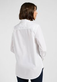 Witte lange mouw shirt met een puntige kraag, knopen manchetten en een ronde zoom, gemaakt van gladde katoen, getoond van achteren.