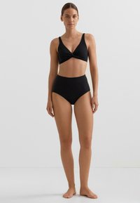 Čierne dvojdielne bikiny, ktoré tvoria bralety s predným prekrížením a širokými ramienkami a plavkové nohavičky s vysokým pásom. Hladká štruktúra a minimalistický dizajn.