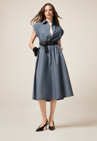 Robe chemise en denim avec des manches courtes, une taille cintrée accentuée par une ceinture noire tressée, et une jupe évasée. Des escarpins noirs à bout pointu complètent le look.
